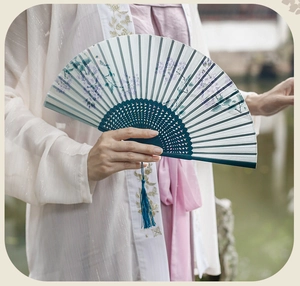 Detail of a Chinese folding fan with purple wisteria patterns and a blue tassel accessory