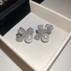 Elegant silver bow earrings with sparkling cubic zirconia and hanging pearls on a beige box