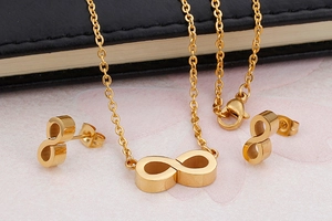 Detailed view of a gold infinity necklace and earring set on a soft pink surface