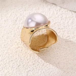 Detail of wide gold textured ring with large cream pearl on a white stone background