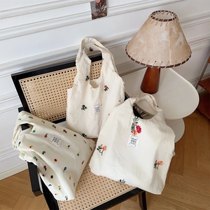 Detail view of off-white canvas tote bags with delicate floral embroidery on a chair