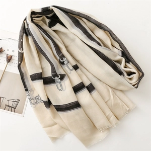 Detail of beige scarf with black chain patterns and tassels on a styled background