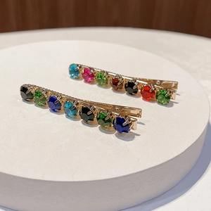 Colorful rhinestone hair clips set with gold plating on a white stone pedestal