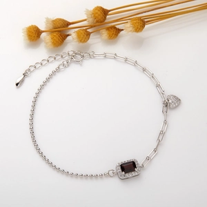 Detail of S925 silver bracelet featuring red square gemstone and heart charm detail