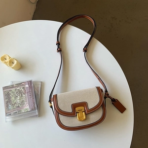 Dettaglio borsa a sella in tela con finiture in pelle marrone e chiusura in metallo