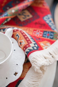 Detail of bohemian red jacquard table runner with fringe and a white ceramic coffee cup