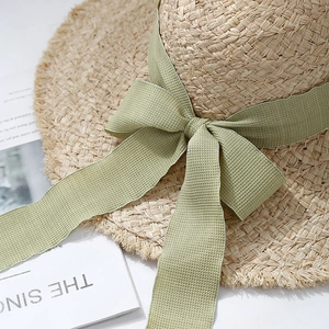 Wide brim raffia straw sun hat with green plaid ribbon bow and frayed edge detailing