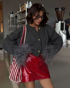 Detail of red patent leather mini skirt paired with grey feather cuff cardigan in a cafe
