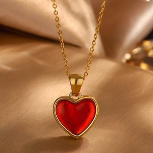 Macro detail of gold-plated chain and red heart pendant on soft golden silk fabric