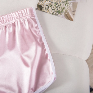 Detail of pink satin lounge shorts with white piping and elastic waistband on a soft surface