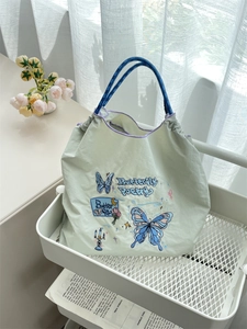 Detail of light green tote bag with blue butterfly embroidery and woven rope handles