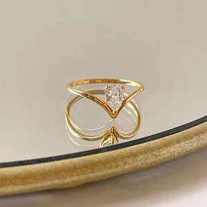 Macro shot of gold V-shaped ring featuring a sparkling pear-cut zircon on mirror base