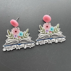 Detail of acrylic book earrings featuring flowers and Just One More Chapter text