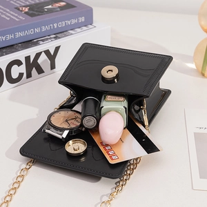 Mini black jelly shoulder bag with gold chain strap shown with essentials on a desk