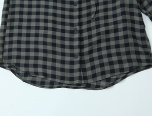 Close-up of the curved hem and button placket on a grey plaid woven shirt