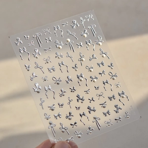 Detailed macro view of 3D silver bow and pearl nail stickers on transparent film