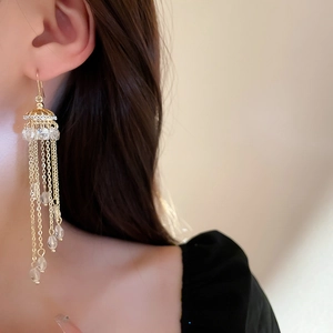 Close-up of elegant gold tassel earrings with crystal droplets on a model's ear