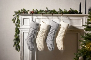 Detail of knitted Christmas stockings with cable patterns and tassels on a mantel