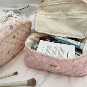 Detail of pink quilted cartoon makeup bag with floral bear patterns on a bed