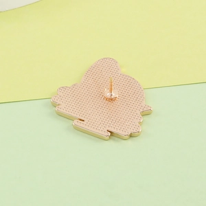 Detailed back view of a gold dinosaur enamel pin with textured finish and safety pin