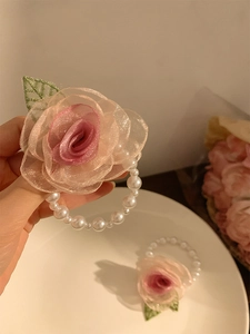 Detail of pink fabric rose hair clip with pearl beads held over white tray background