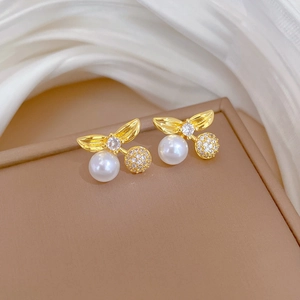 Detailed macro shot of cherry-shaped gold stud earrings with white pearl and zircon accents