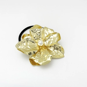 Detail of golden metal flower hair tie with hammered petals and a white pearl accent