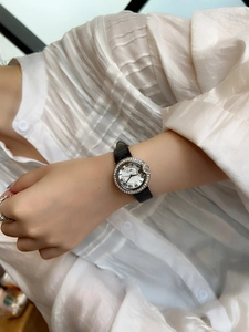 Detail shot of a silver oval quartz watch with rhinestones on a black leather strap