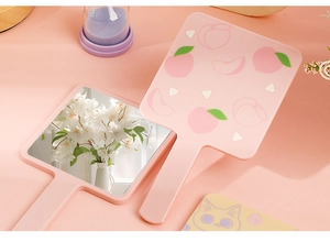 Close-up of pink handheld makeup mirror featuring a cute peach pattern and handle