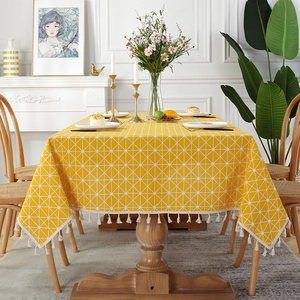 Detail of yellow geometric mesh tablecloth with decorative tassels on a wooden table