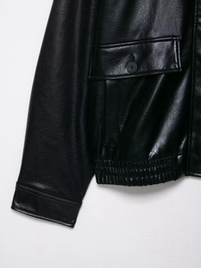 Detail of black faux leather bomber jacket showing pocket stitching and texture