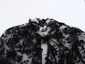 Detail of sheer black lace blouse featuring a floral pattern and elegant tie-neck collar