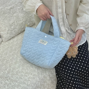 Detail of light blue heart quilted handbag with brown plush bear charm and woven label
