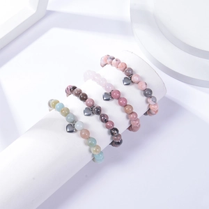 Macro shot of 8mm natural stone bracelets with silver heart pendants on white stands