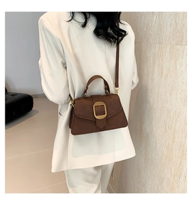 Close-up of brown vintage square bag with oversized golden buckle and textured finish