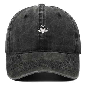 Macro detail of white bee embroidery on dark grey washed denim baseball cap fabric