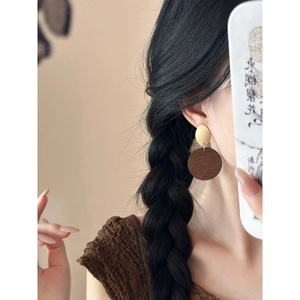 Retro round wood pendant earrings with gold oval metal studs worn by a model