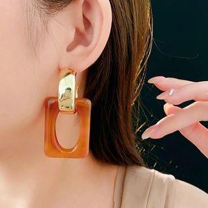 Close-up of geometric C-shaped golden earrings with large tortoiseshell resin pendants