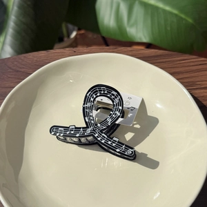 Detail of a black hair claw clip with musical notes placed on a beige ceramic plate