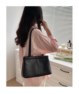 Side view of a black minimalist leather tote bag worn by a model in a bright room