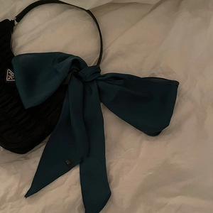 Detail of a black pleated handbag adorned with a large dark green silk scarf ribbon tie