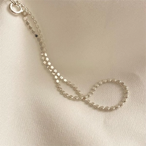 Detailed close-up of S925 sterling silver flat bead anklet on soft beige silk