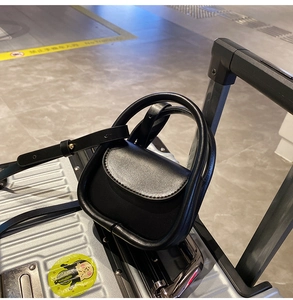 Mini sac noir en bandoulière accroché à la poignée d'une valise en voyage