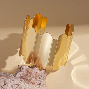 Detail of a wide gold cuff bracelet featuring a geometric ridged design on a rock base