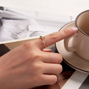 Close-up of golden cat ring with pink heart stone worn by a model holding a coffee cup