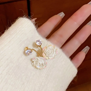 Detail of rose-shaped earrings with white resin petals and gold metal frame