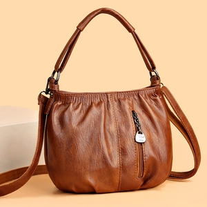 Brown soft leather pleated handbag with shoulder strap and front zipper on beige backdrop