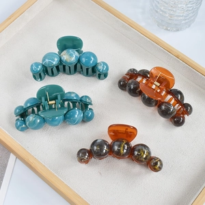 Detail view of large marble texture hair claws in amber and turquoise on a tray