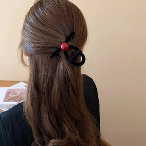 Close-up of elegant black flocked claw clip with a red bead on long brown wavy hair