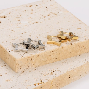 Star-shaped stainless steel hoop earrings in gold and silver on beige stone